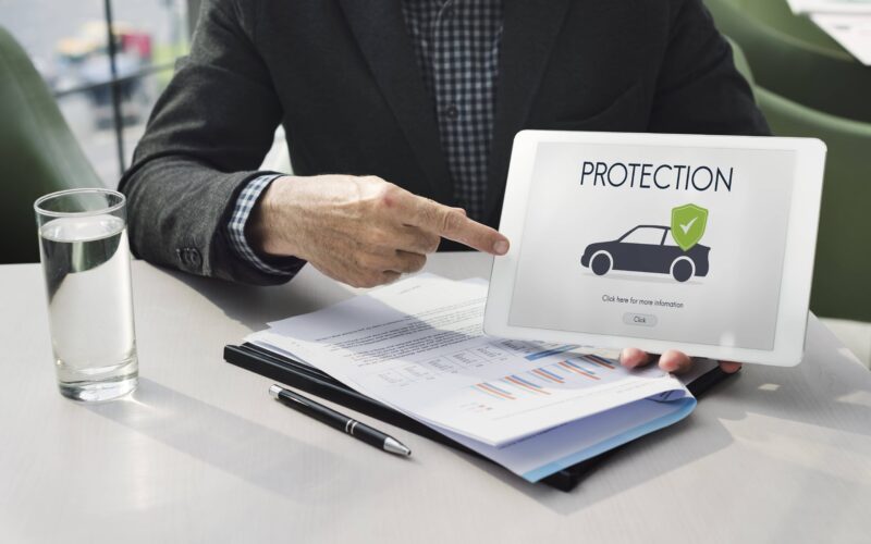 Insurance professional pointing to a tablet screen displaying car protection information over documents