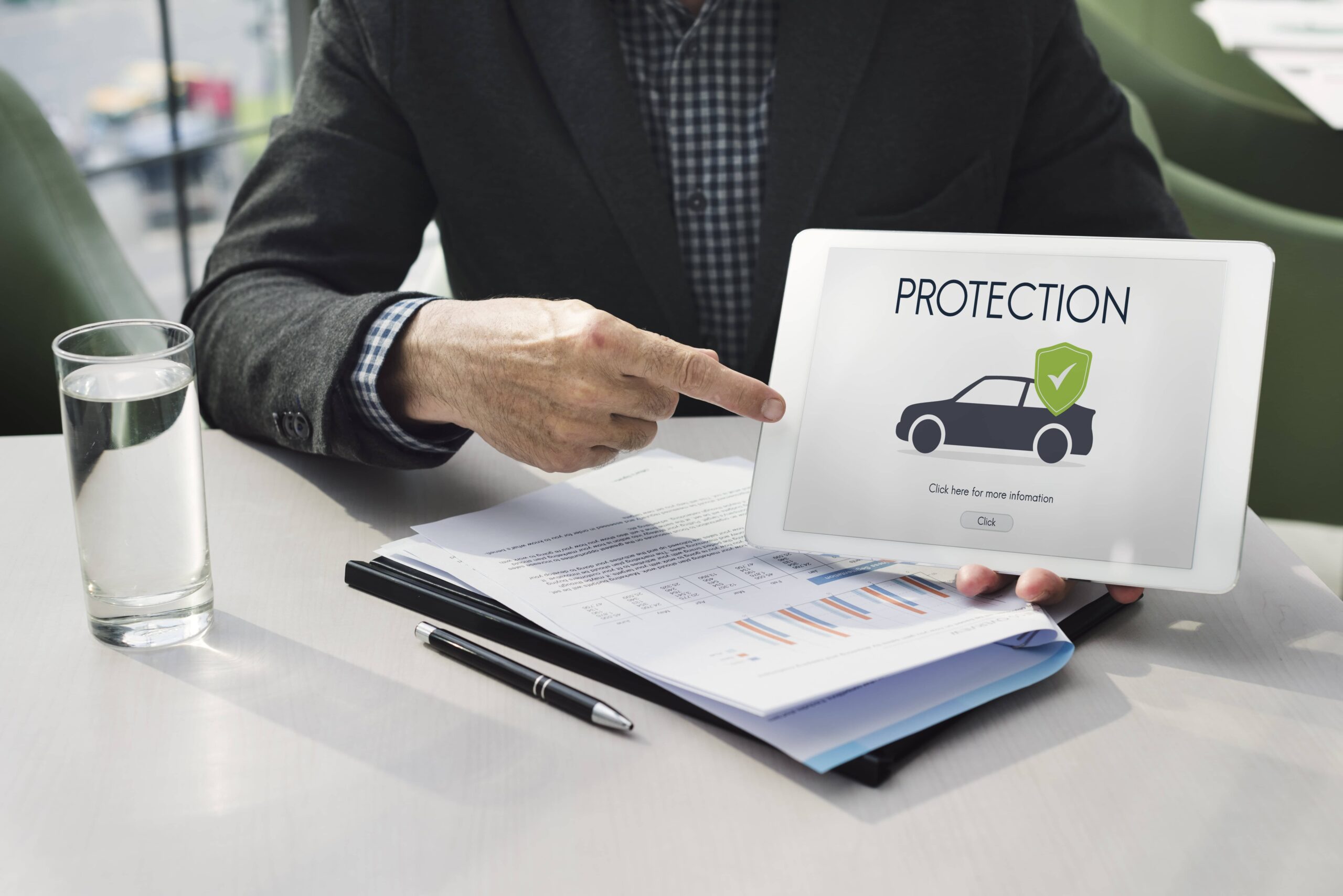 Insurance professional pointing to a tablet screen displaying car protection information over documents