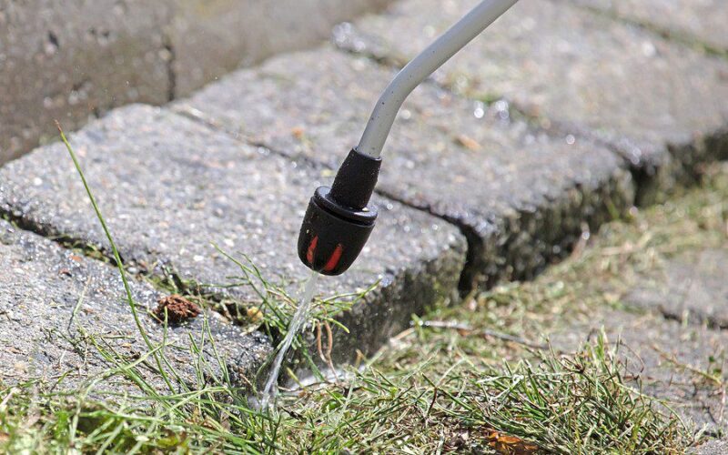 Close-up of a weed sprayer applying herbicide between paving stones